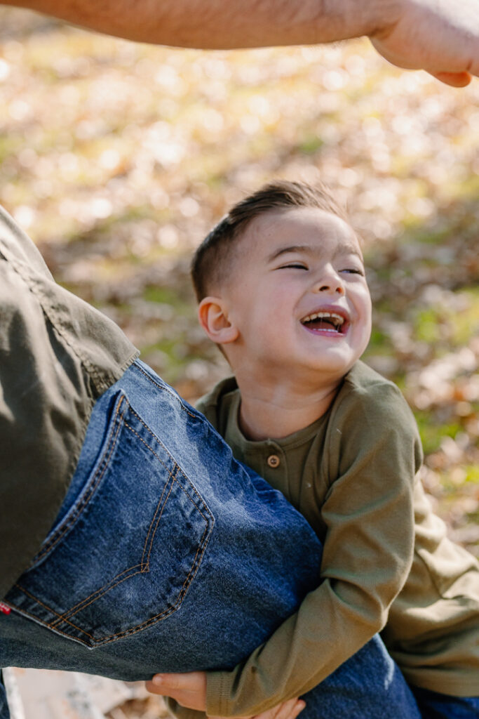 Young boy holding dad's leg and smiling in Oak Glen, CA for photoshoot. 